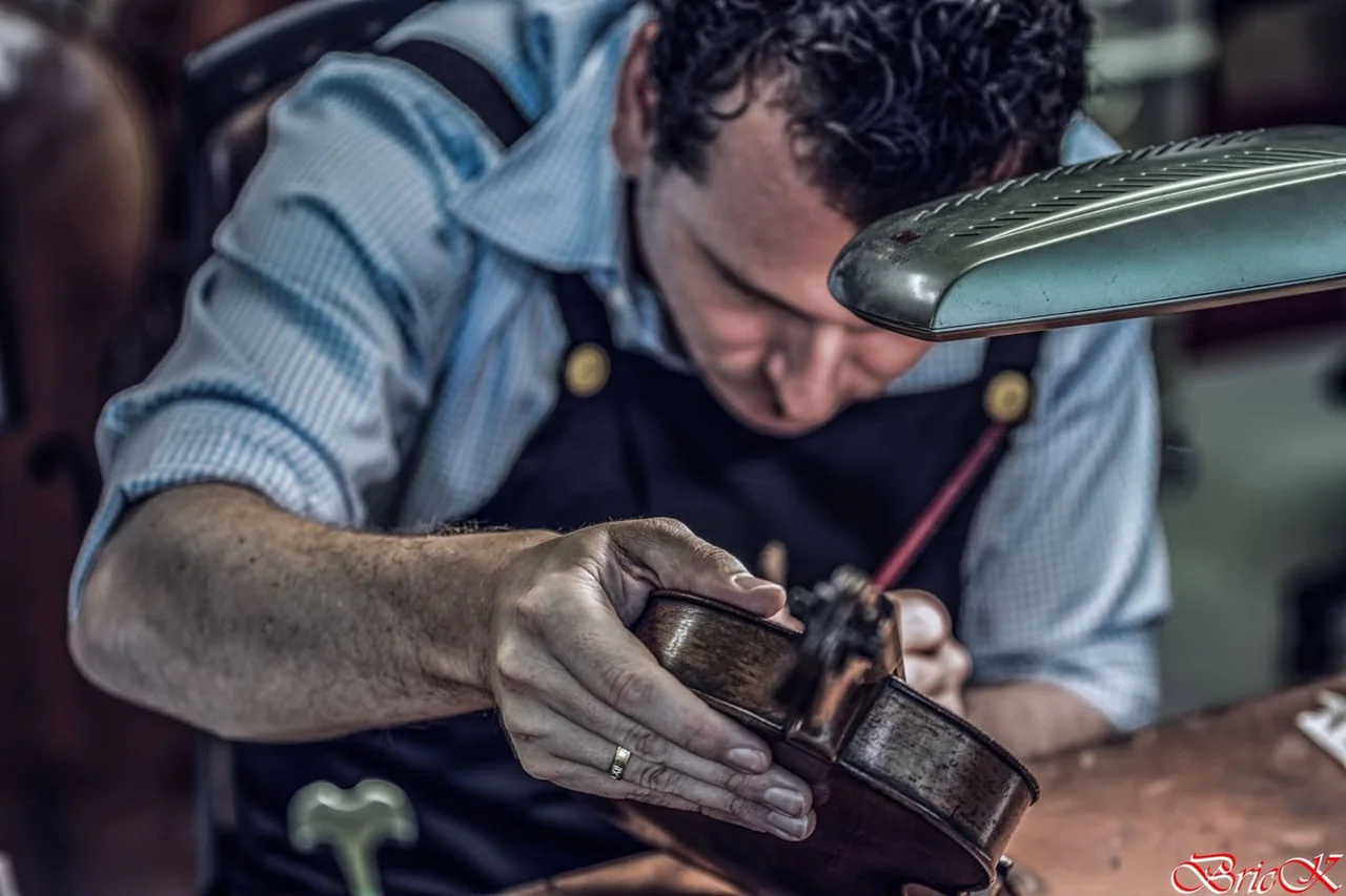A craftsman concentrates on an object held close in his hands.