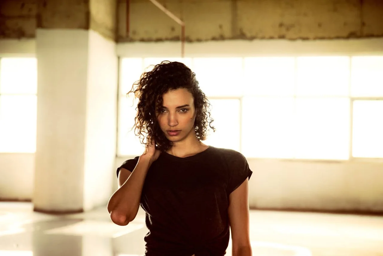 Curly-haired subject in a black shirt against bright loft windows.