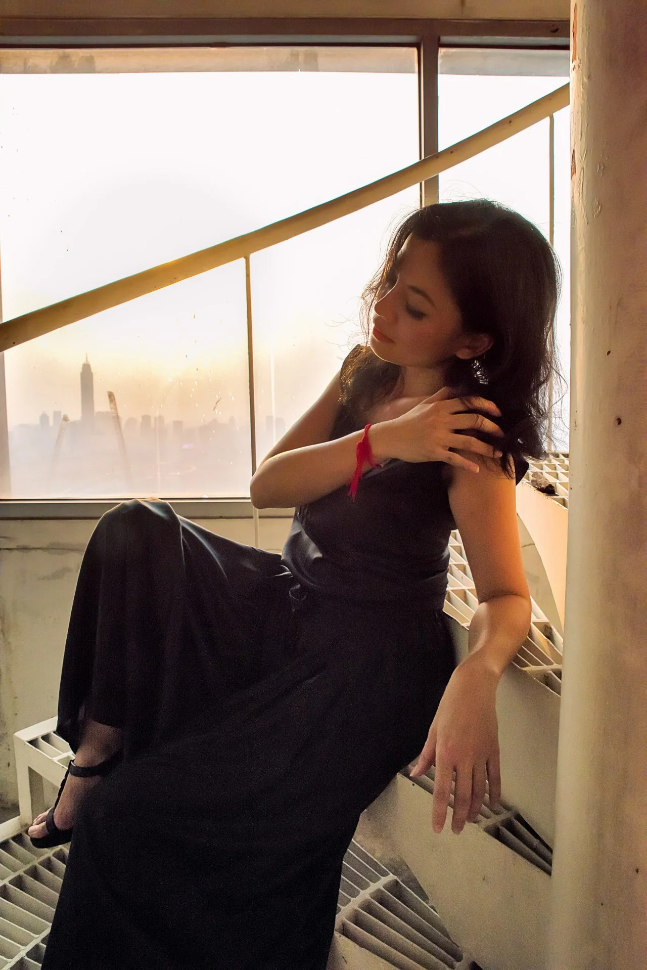A seated woman in a dark gown in warm window light.