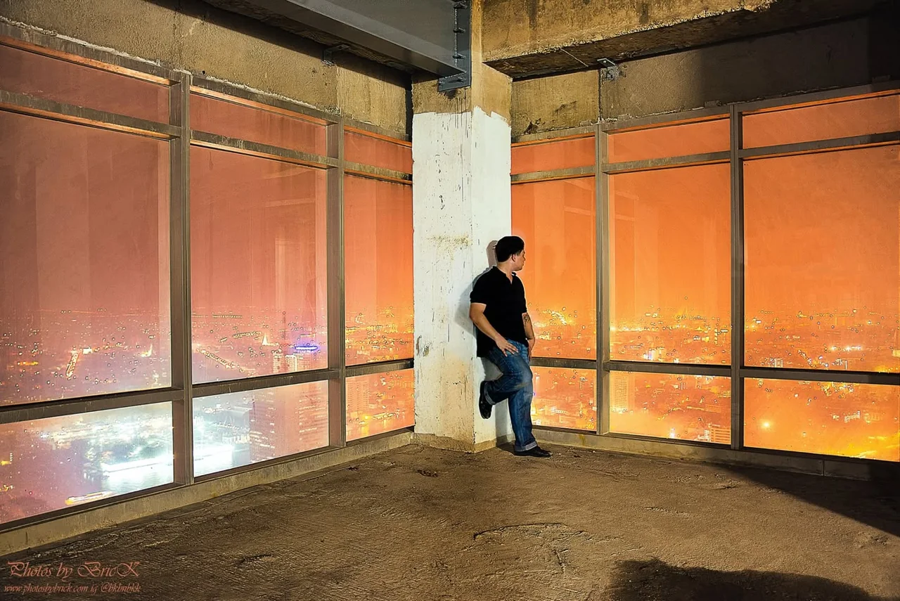 A man leans against a column in a room filled with orange window light.