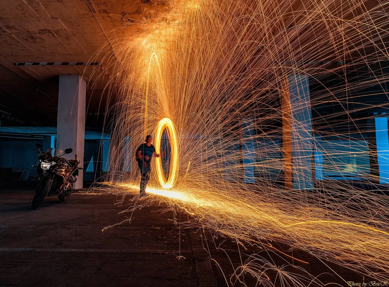 A circle of golden sparks bursts through a dark industrial room.