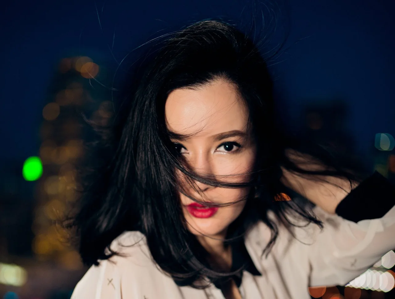 A windblown portrait with a direct gaze against night city lights.
