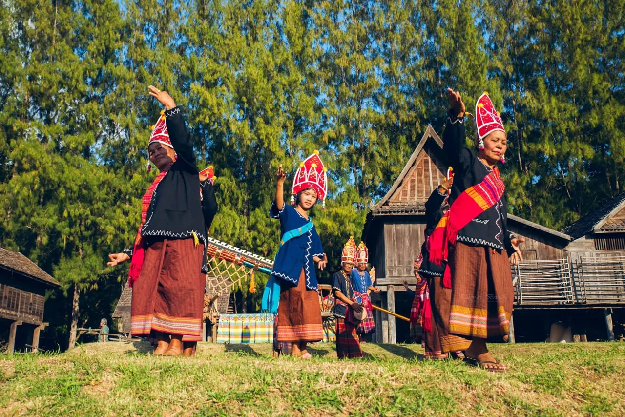 A group performs outdoors in vivid clothing against trees and wooden buildings.