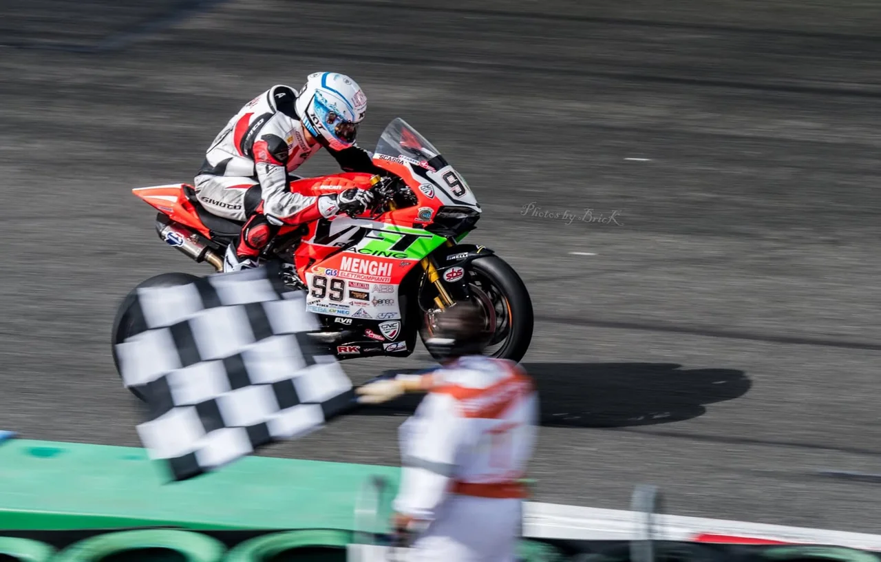 A motorcycle racer passes a blurred checkered flag.