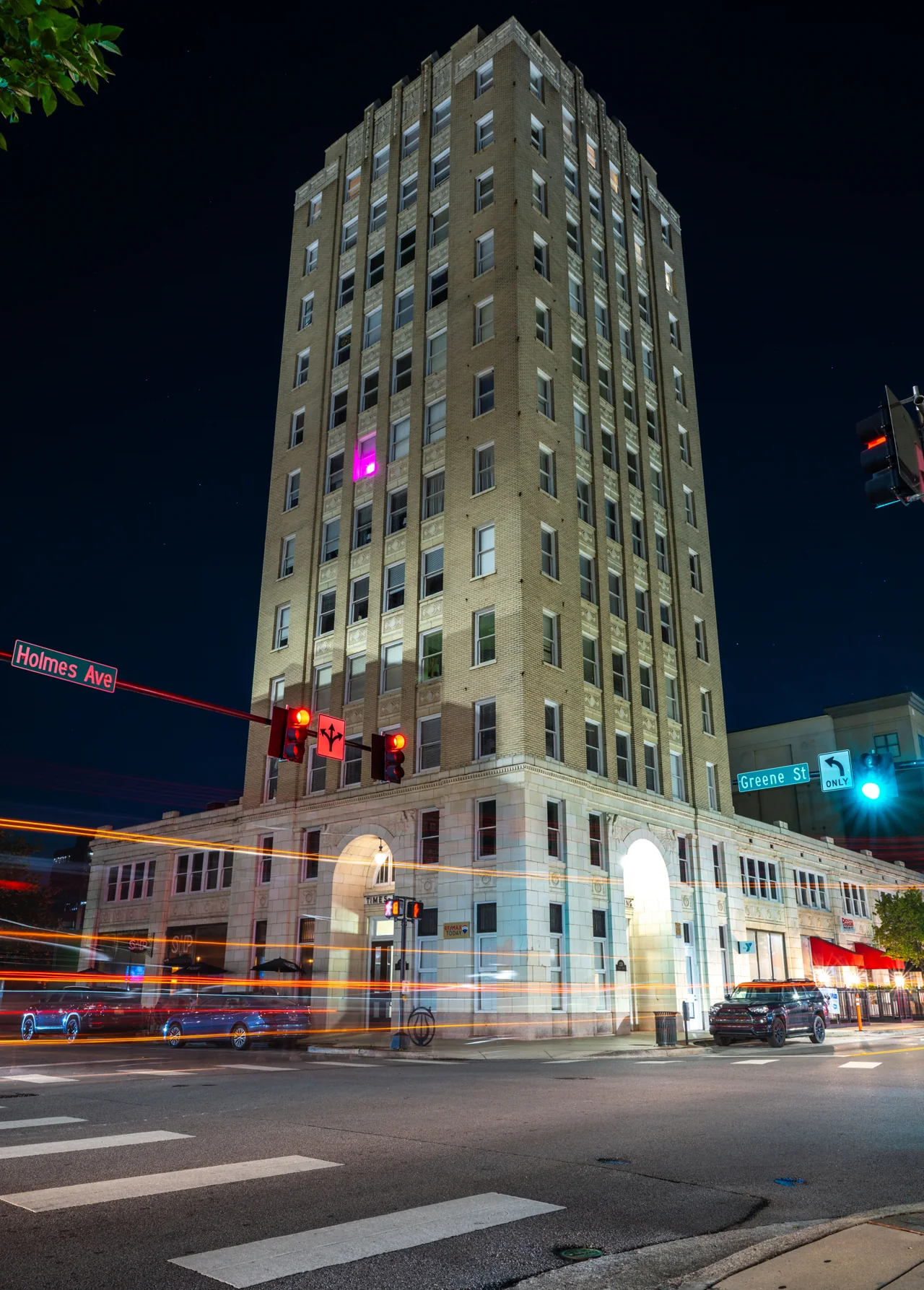 A tall illuminated building rises above red and white traffic trails at night.