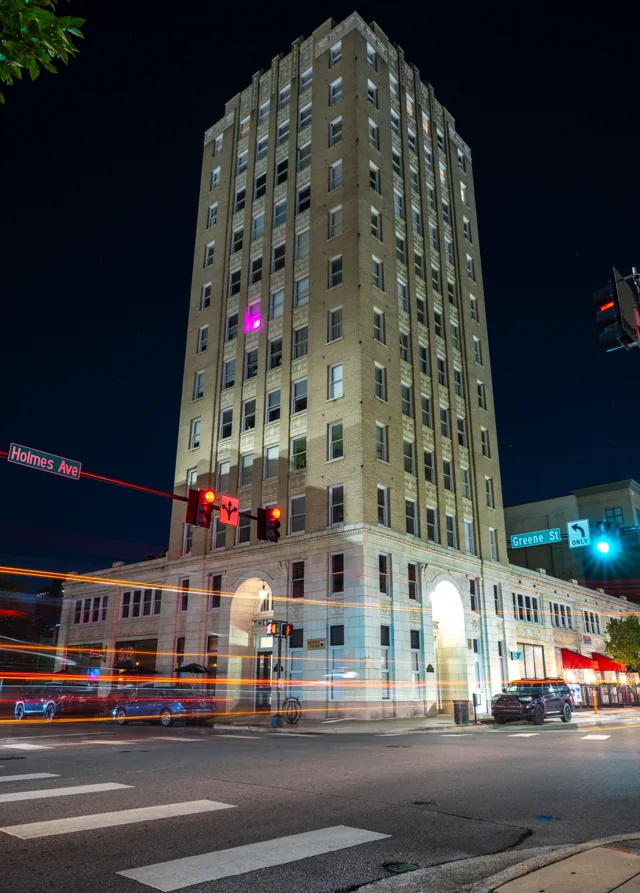 A tall illuminated building rises above red and white traffic trails at night.