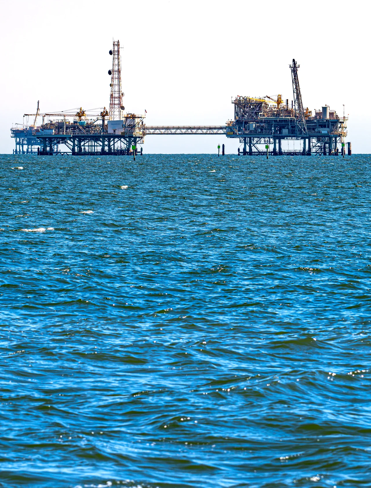 An offshore industrial structure rises from blue water.