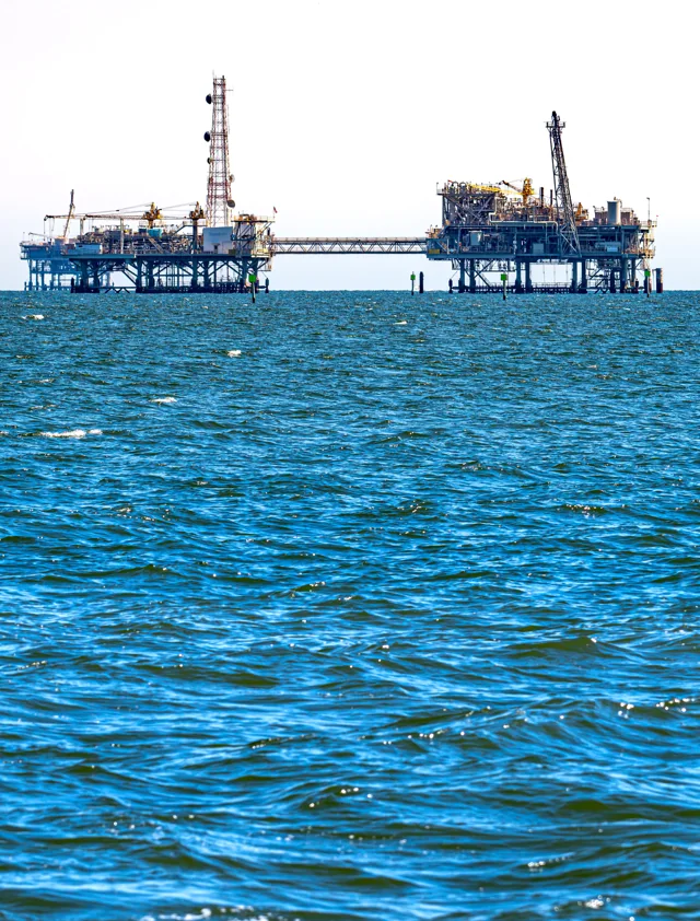 An offshore industrial structure rises from blue water.