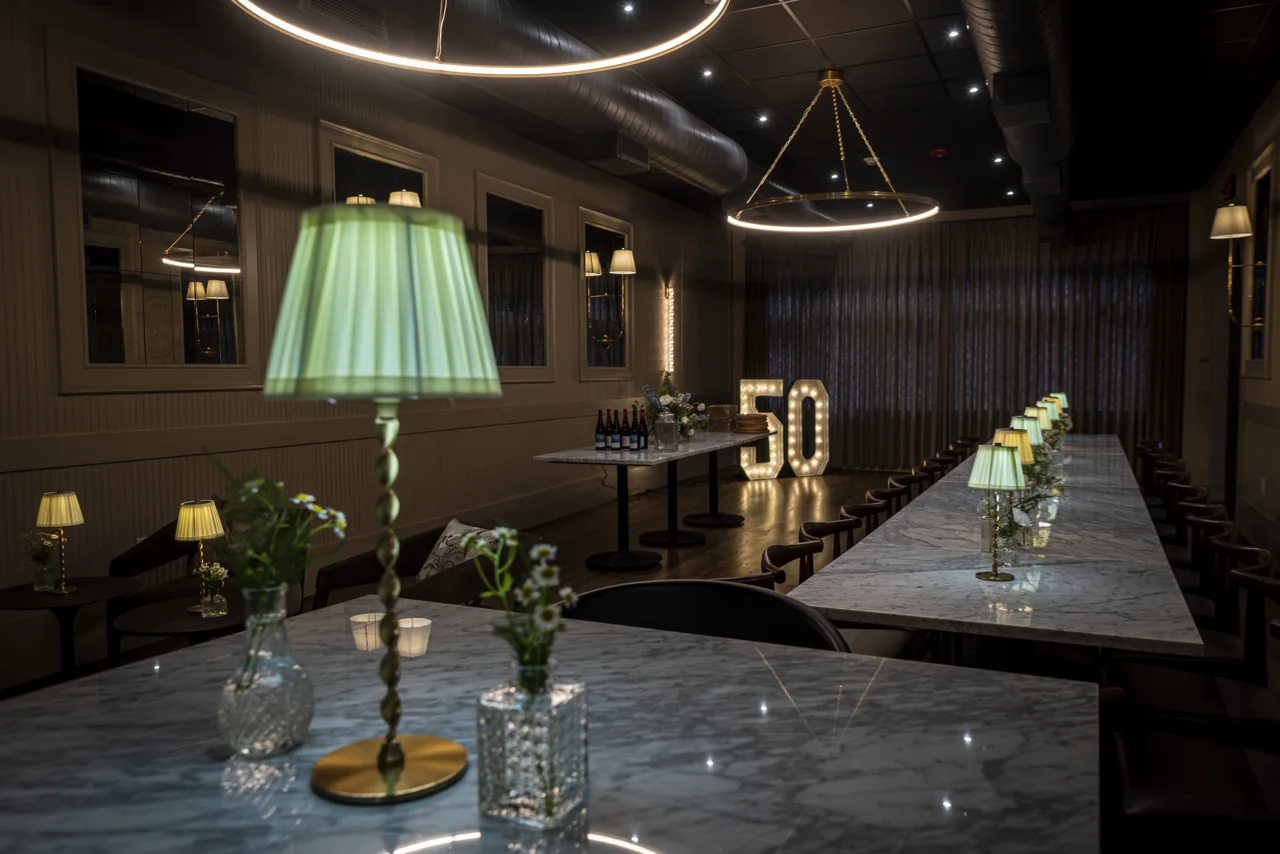 A pale green table lamp glows above a restaurant table and glasses.