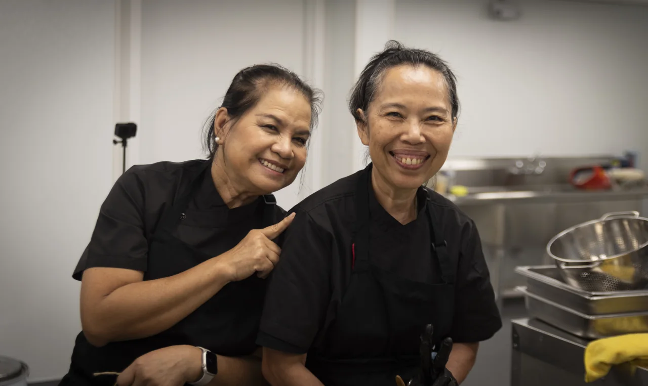 Two smiling members of a kitchen team stand together at work.