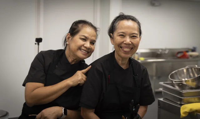 Two smiling members of a kitchen team stand together at work.