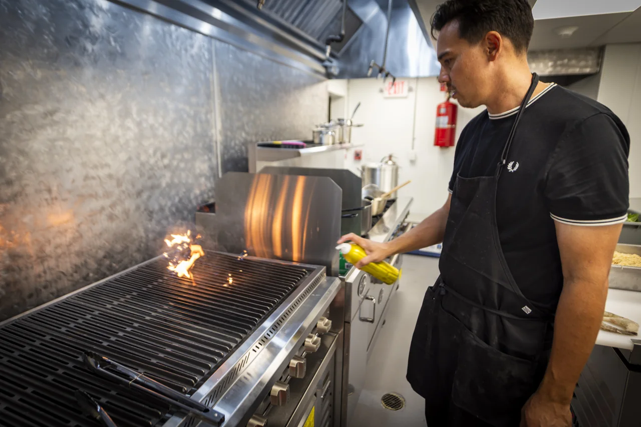 A chef works beside a hot grill in a restaurant kitchen.