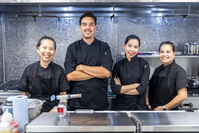 Four chefs stand together behind a kitchen counter.