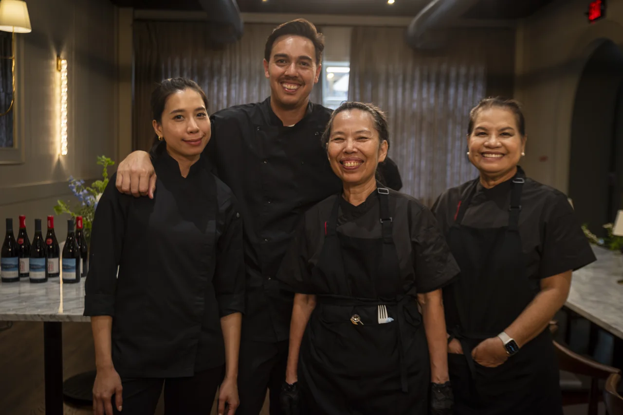 Four chefs stand together inside a warmly lit restaurant.