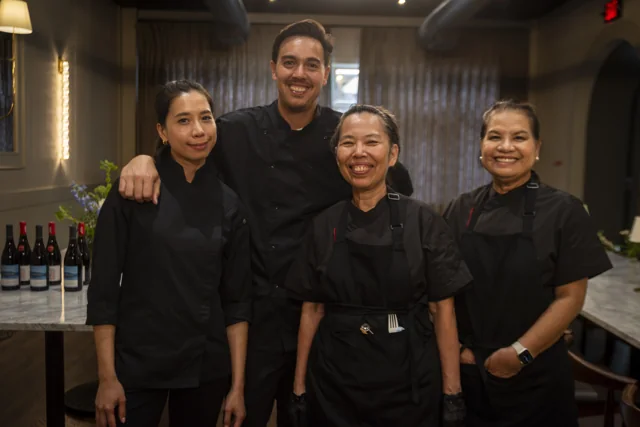 Four chefs stand together inside a warmly lit restaurant.
