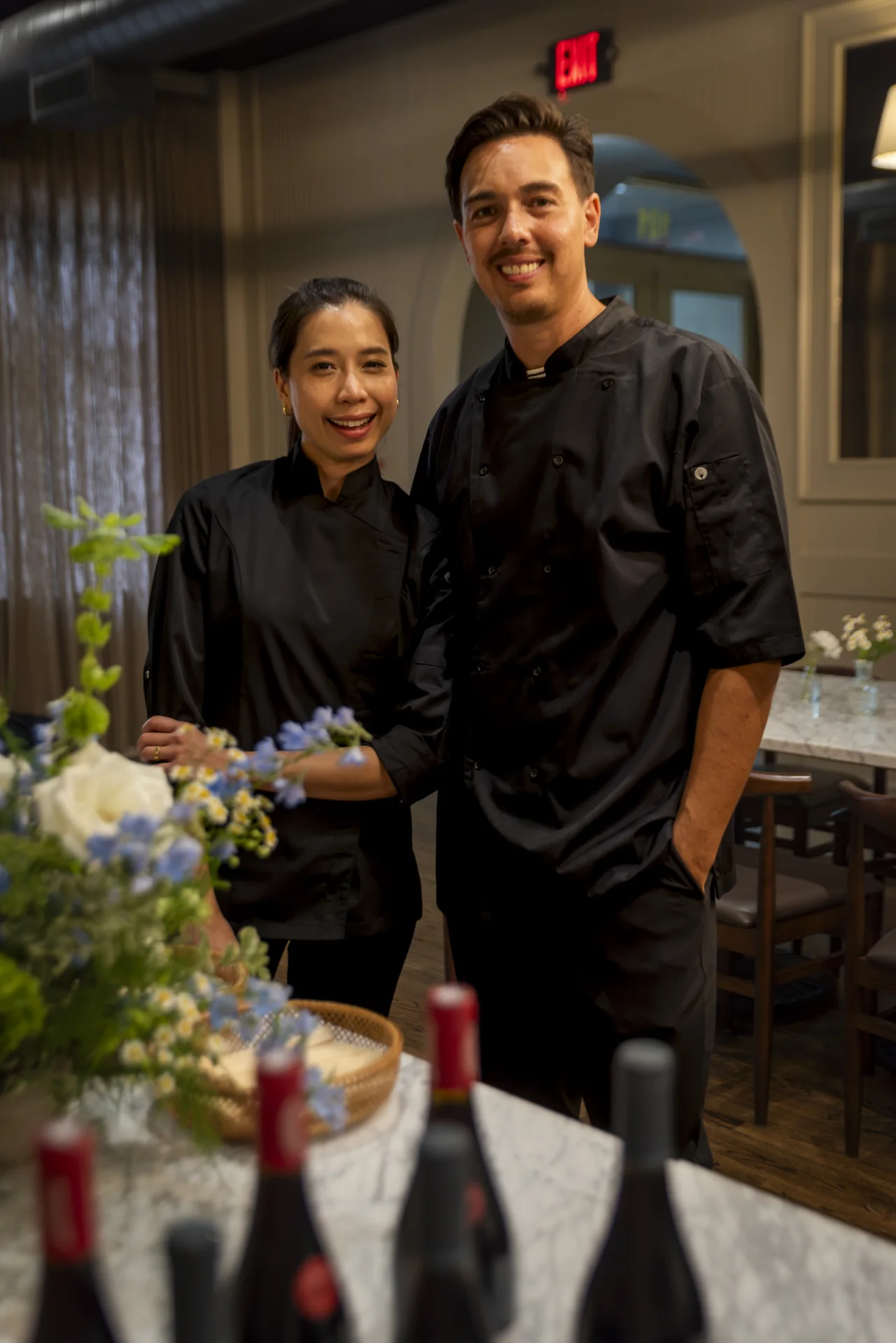 Two chefs stand behind a table of finished dishes.