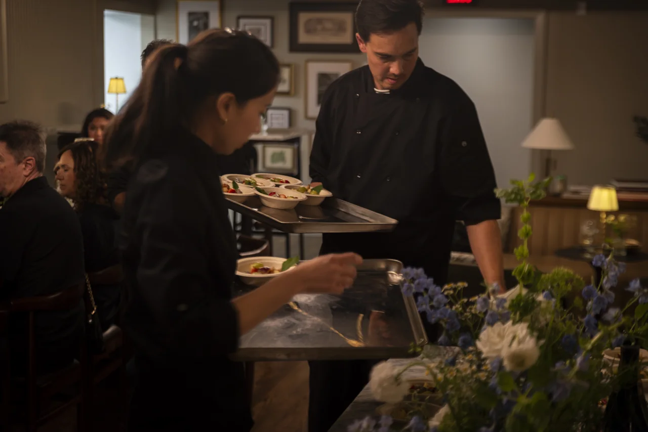 Two members of staff prepare a table set with flowers and small lamps.