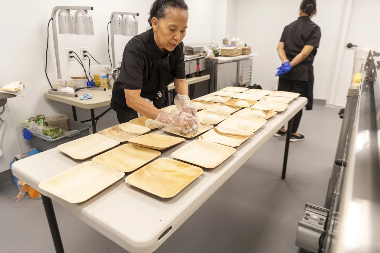 A chef portions food into trays at a kitchen counter.