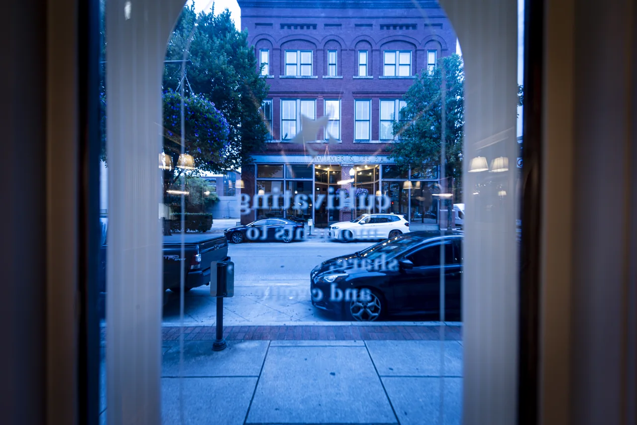A window frames a blue evening street from inside a restaurant.