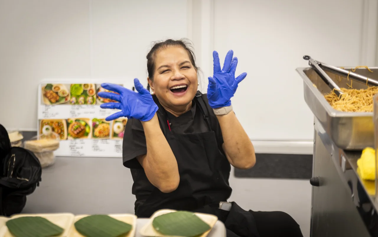 A laughing chef raises blue-gloved hands in the kitchen.