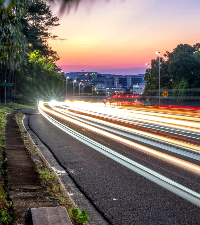 White light trails sweep downhill beneath a pink and orange evening sky.