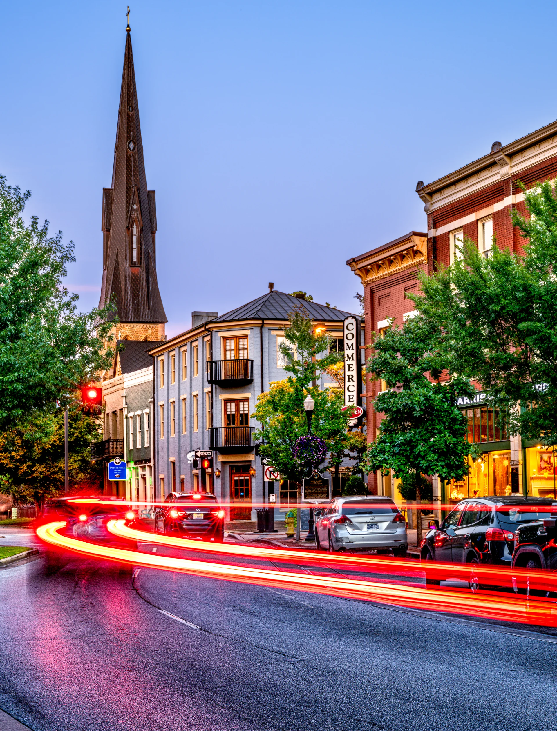 Red traffic trails lead through a city street beneath church spires at blue hour.