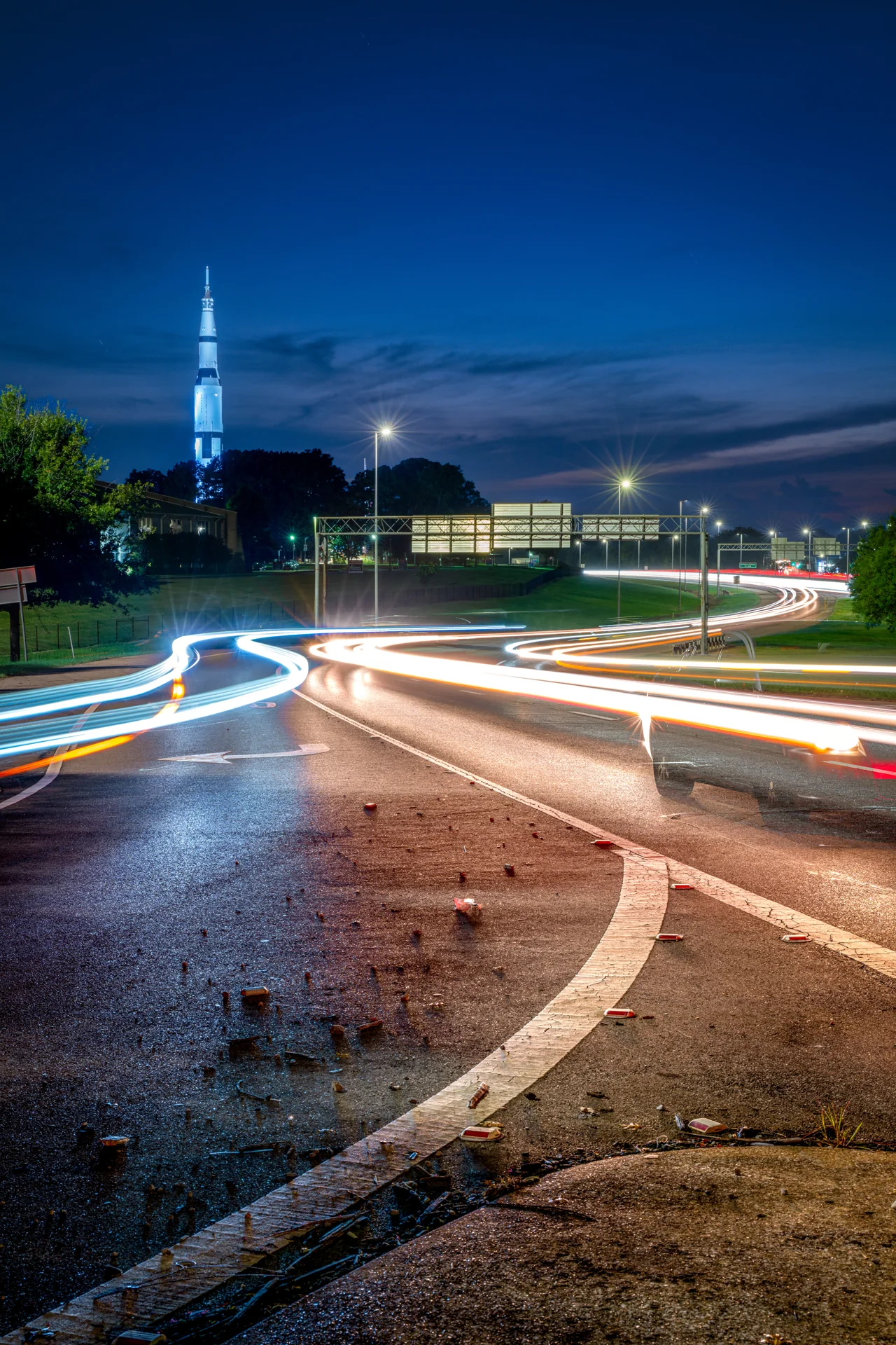 White and red light trails curve across a wet road beneath a deep blue evening sky.