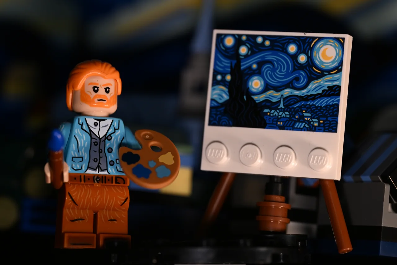 A small toy painter stands beside an easel and a blue swirling painting.