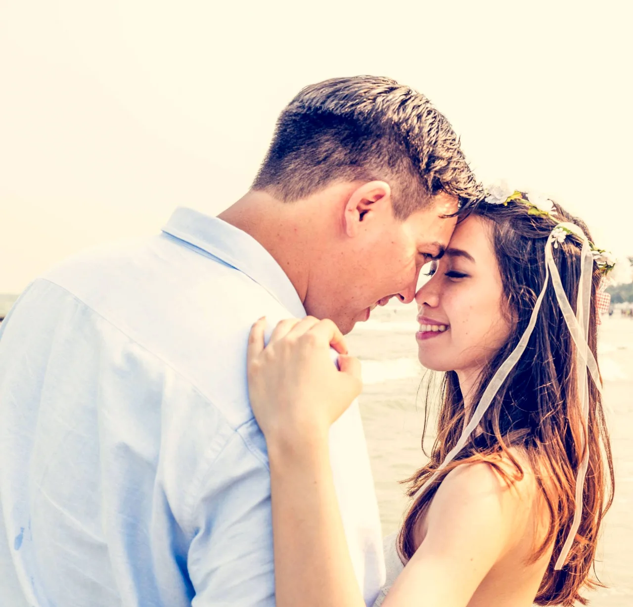 A couple in white clothing lean their foreheads together.
