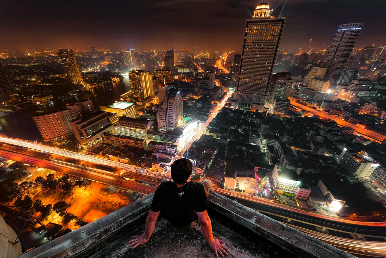 A person sits high above a brightly lit city at night.