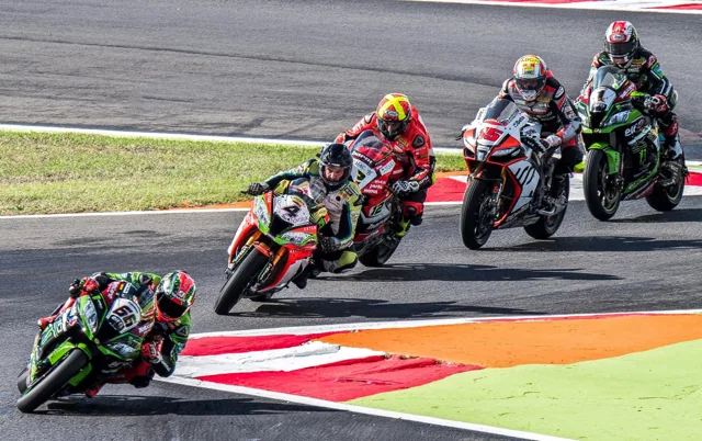 A pack of motorcycle racers lean into a track corner.