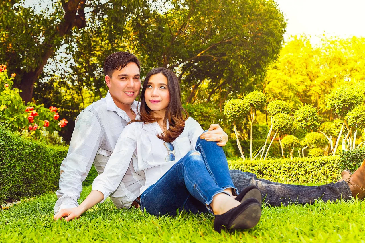 A couple sit together on grass scattered with yellow leaves.