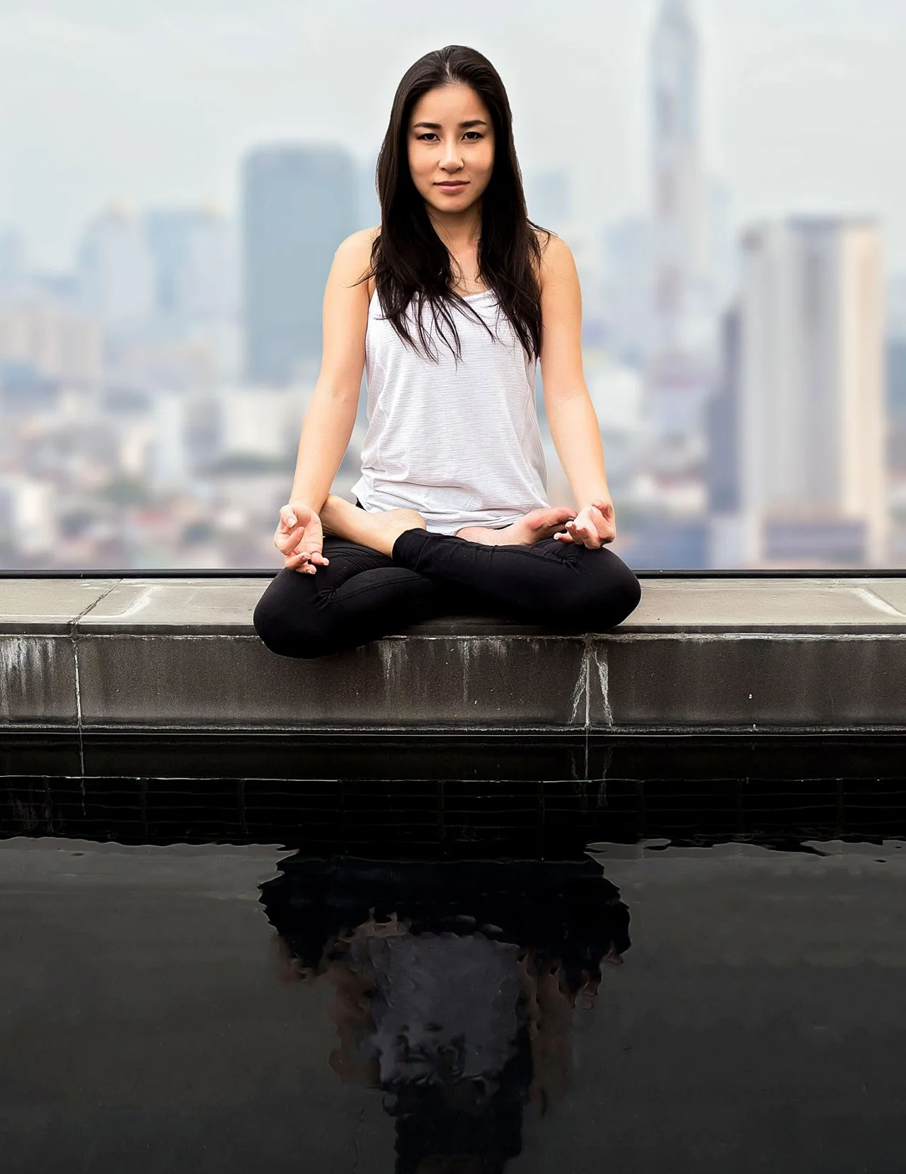 A woman in a white top sits above a dark reflection with a city behind her.