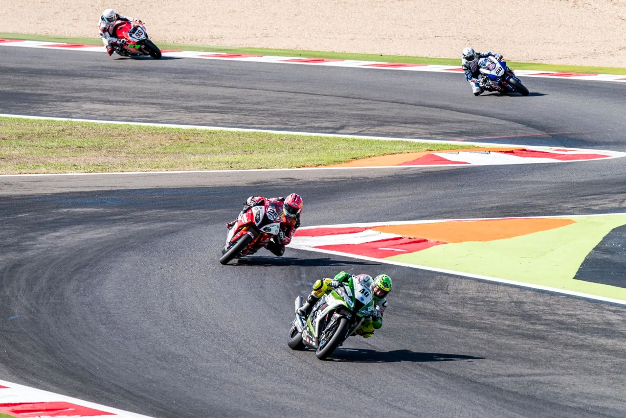 Motorcycle racers follow a broad curve of a race circuit.