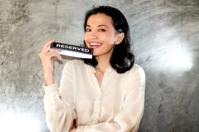 A smiling woman in a white coat holds a small black Reserved sign.