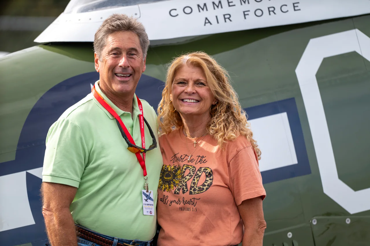 A smiling couple share a close portrait beside an aircraft.