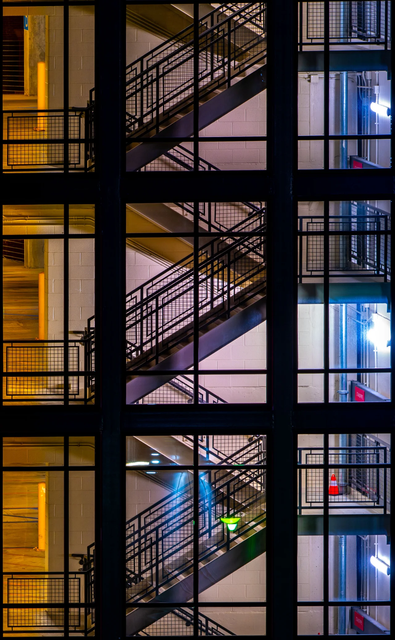 A grid of glass windows frames warm yellow and cool blue stairways.